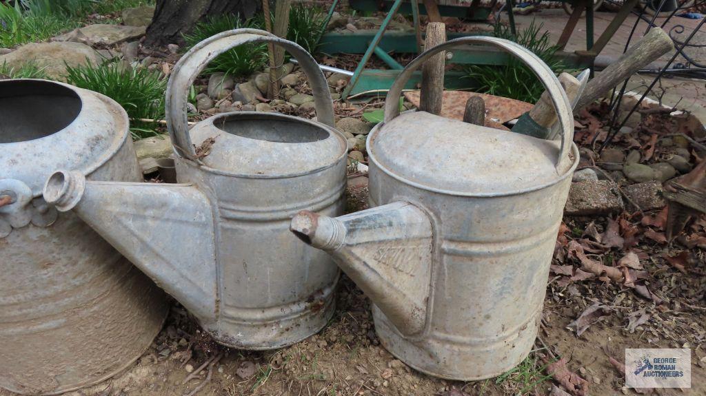 Three vintage watering cans with hand tools