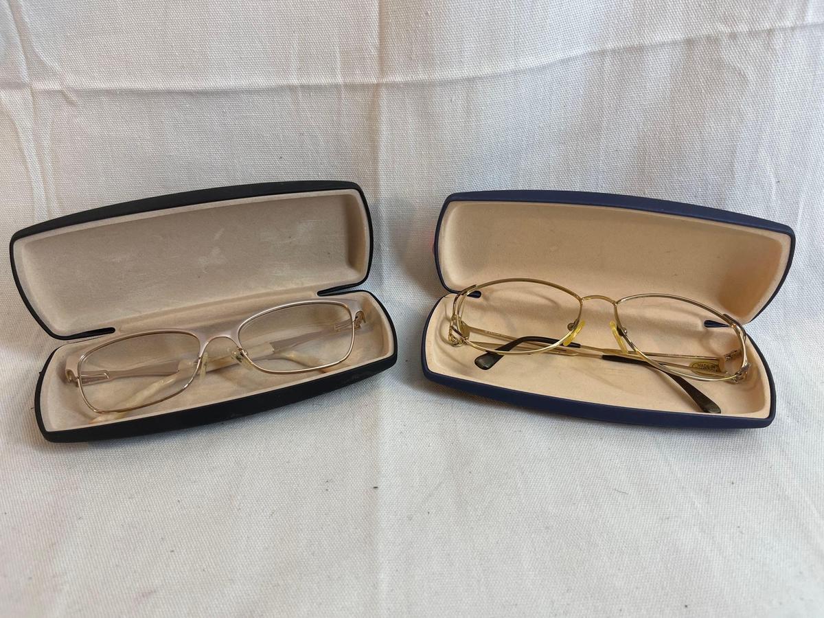 Two eyeglass frames. One has bifocal lenses. The other has no lenses. With cases....